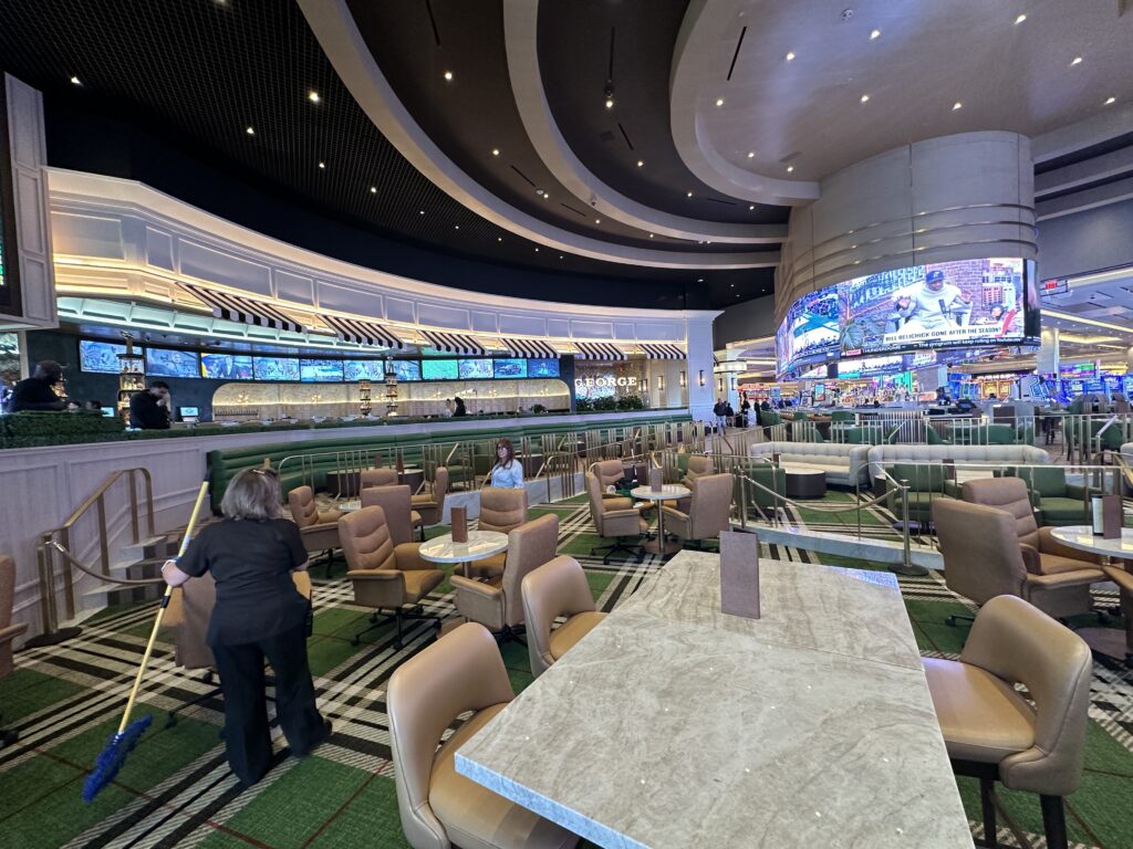 A view from inside the sportsbook facing the bar with wraparound screen on top of it at the entrance.