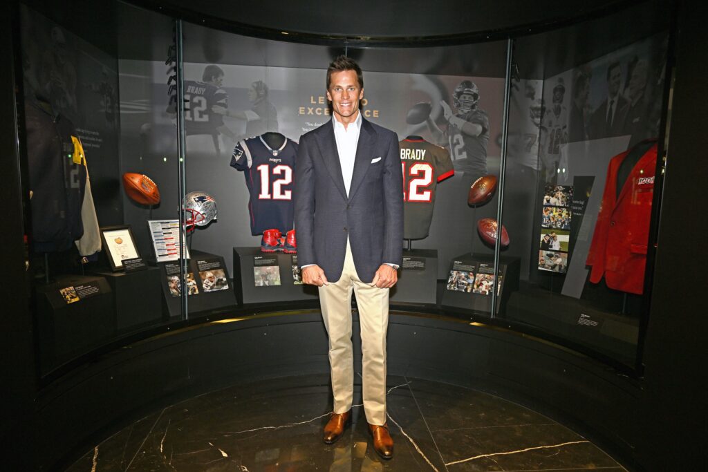 Tom Brady, standing in front of sports memrobelia in the Hall of Excellence.