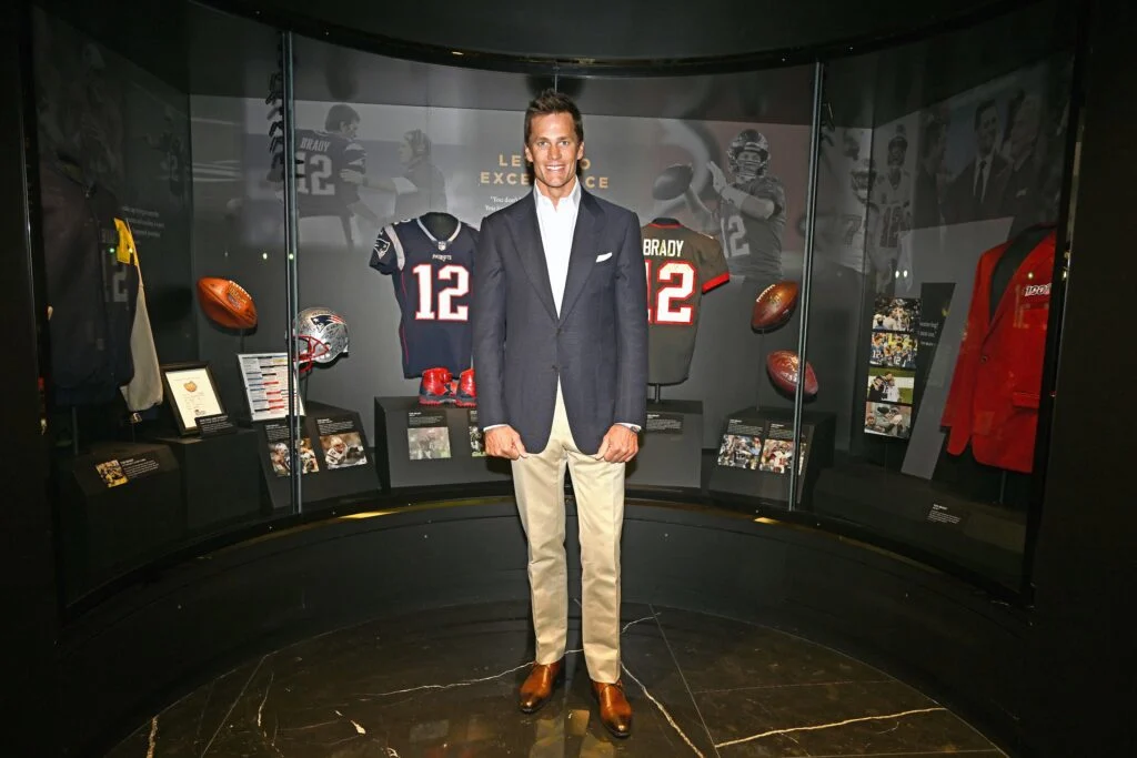 Tom Brady, standing in front of sports memrobelia in the Hall of Excellence.