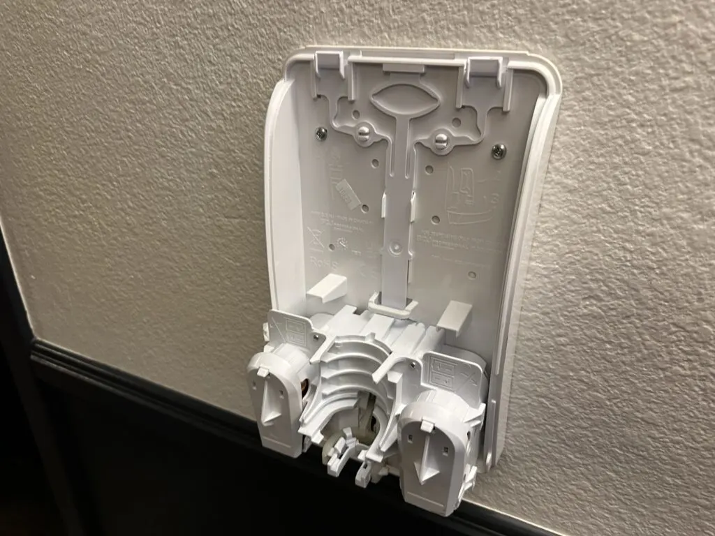 A busted up remnant of a hand sanitizer dispenser on the wall. 