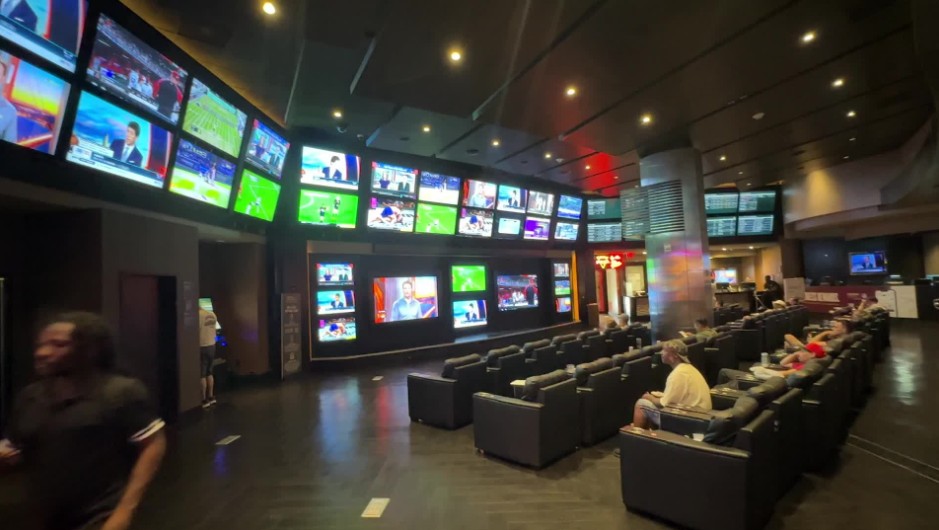 A small sportsbook with a lot of LED TVs hanging on the wall and about 20 chairs. 