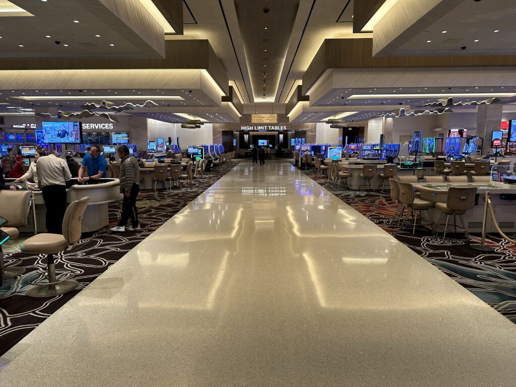 An empty walkway cuts between two banks of table games on either side and leads to the high limit room.