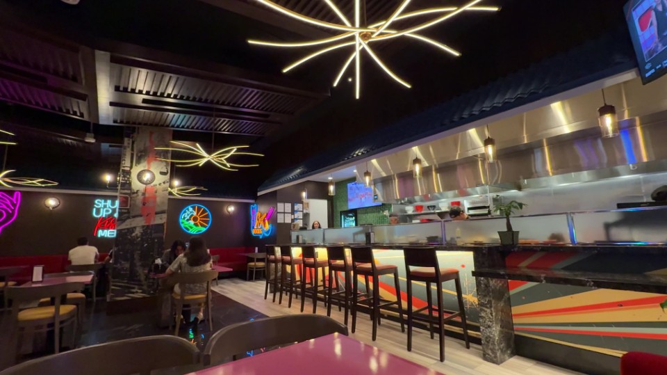 The inside of Hot Noods, which shows bar seating to the right and neon decor on the ceiling and walls .
