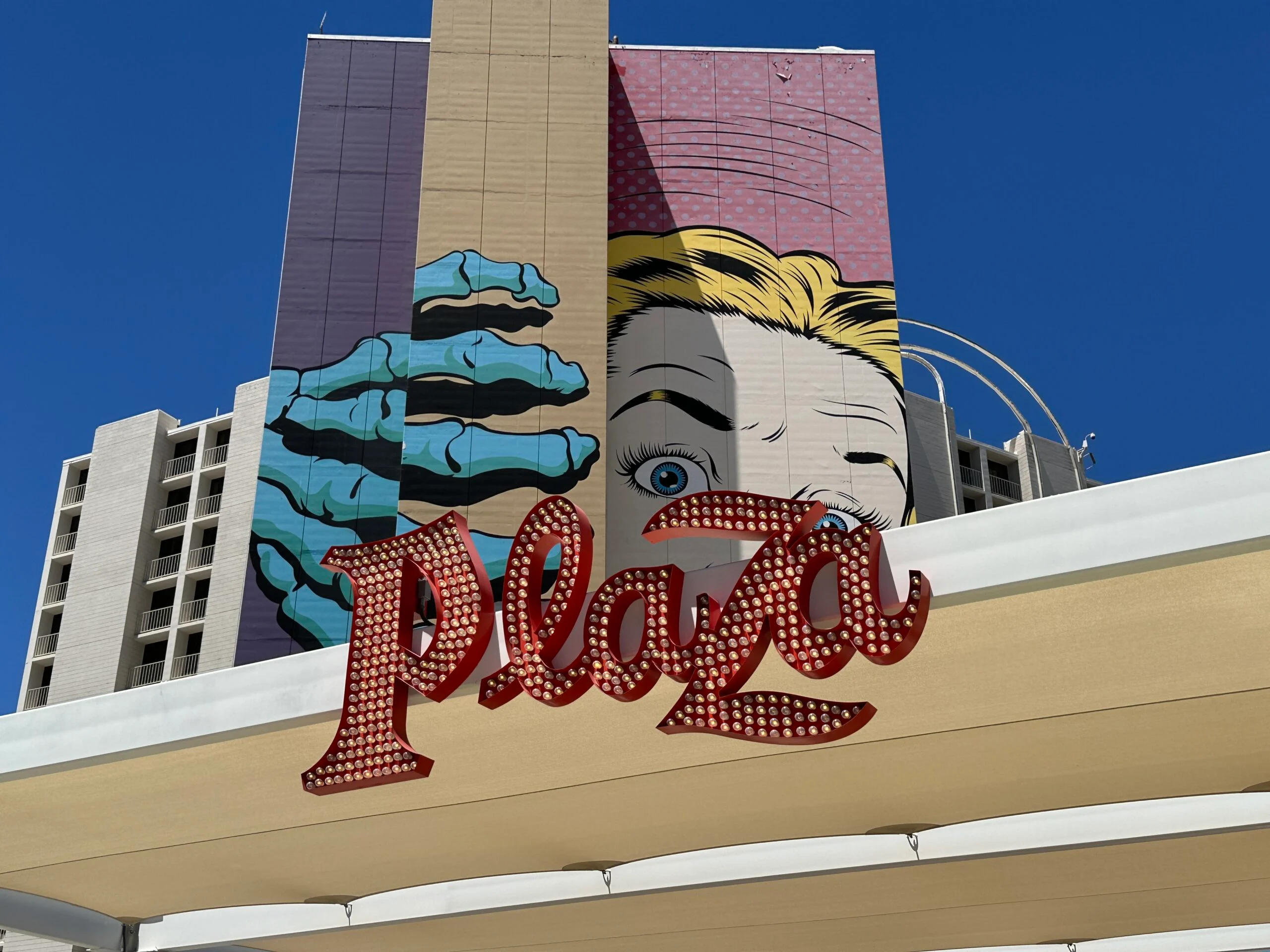 A red sign says Plaza hangs in front of D*Face's mural on the north tower of a monster opening a door. A scared women is behind the door.