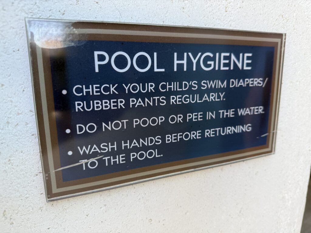 Sign titled 'POOL HYGIENE' with bullet-point pool safety and hygiene guidelines on a blue plaque mounted to a textured wall.