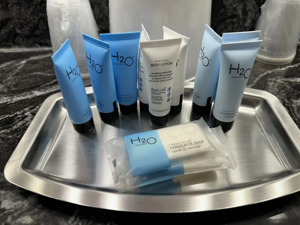 A hodgepodge of bath produccts sloppily placed on a silver tray on the bathroom counter.