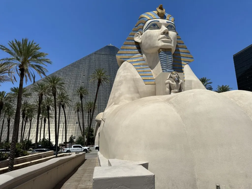 The exterior of Luxor Las Vegas. A sphinx is in the foreground while the black pyramid shaped tower peeks out from behind.