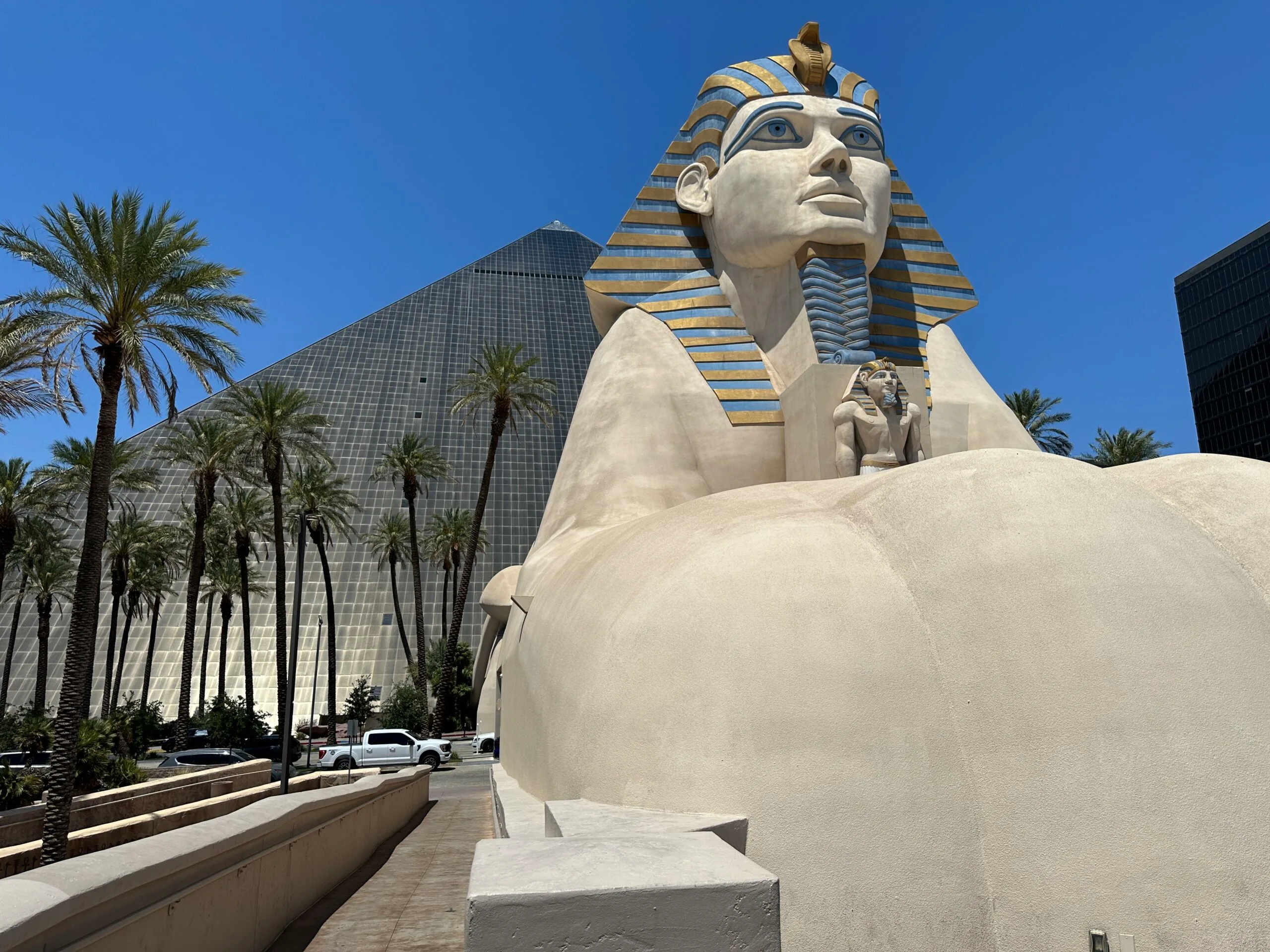 The exterior of Luxor Las Vegas. A sphinx is in the foreground while the black pyramid shaped tower peeks out from behind.