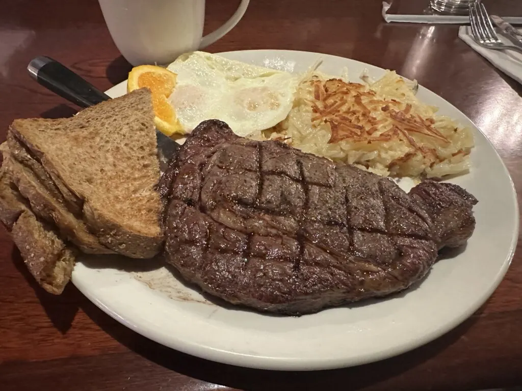 A ribeye steak, toast, eggs over easy, and hashbrowns on a white plate.