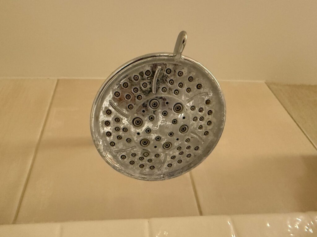 A showerhead with a white crust on the surface. 