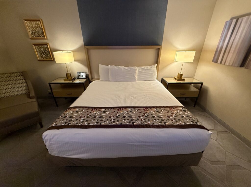 The king bed seen from the foot of the bed, with a gray/blue accent wall above the headboard. 