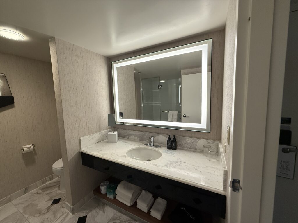 An illuminated mirror above a single sink vanity. 