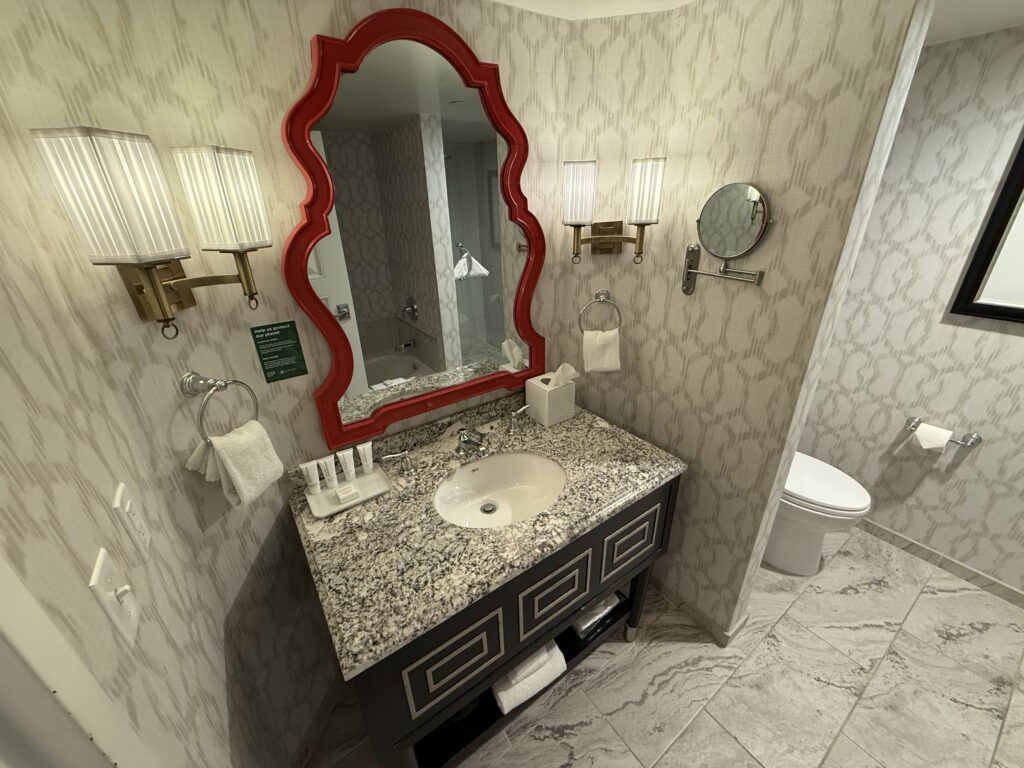 The bathroom vanity, which has one sink, and a red trimmed mirror above. 