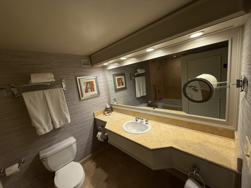 A single sink vanity, with a large mirror above next to a toilet. 