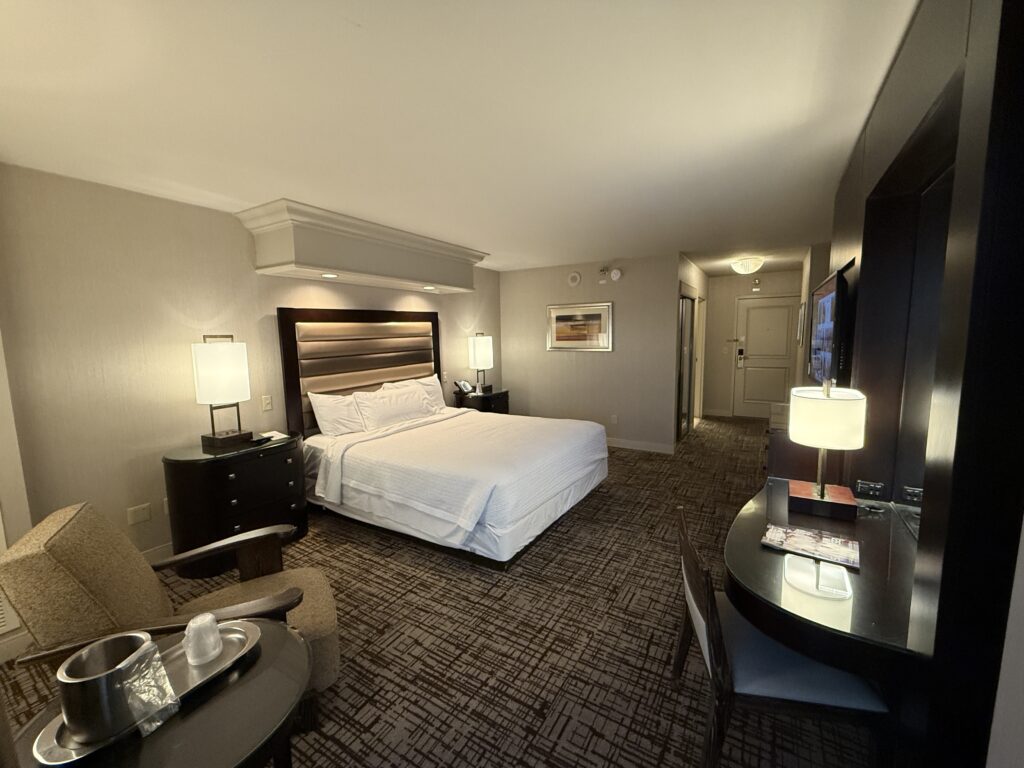 Wide angle shot of room at TI with a king bed up against a padded headboard, which is underneath can lights. 