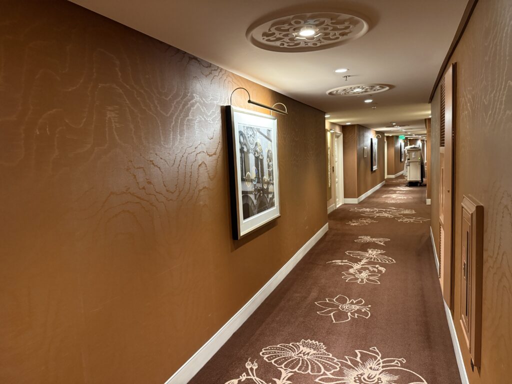 A hotel hallway lined with illuminated arwork on the walls. The color scheme is brown and creme - Wynn's colors. 