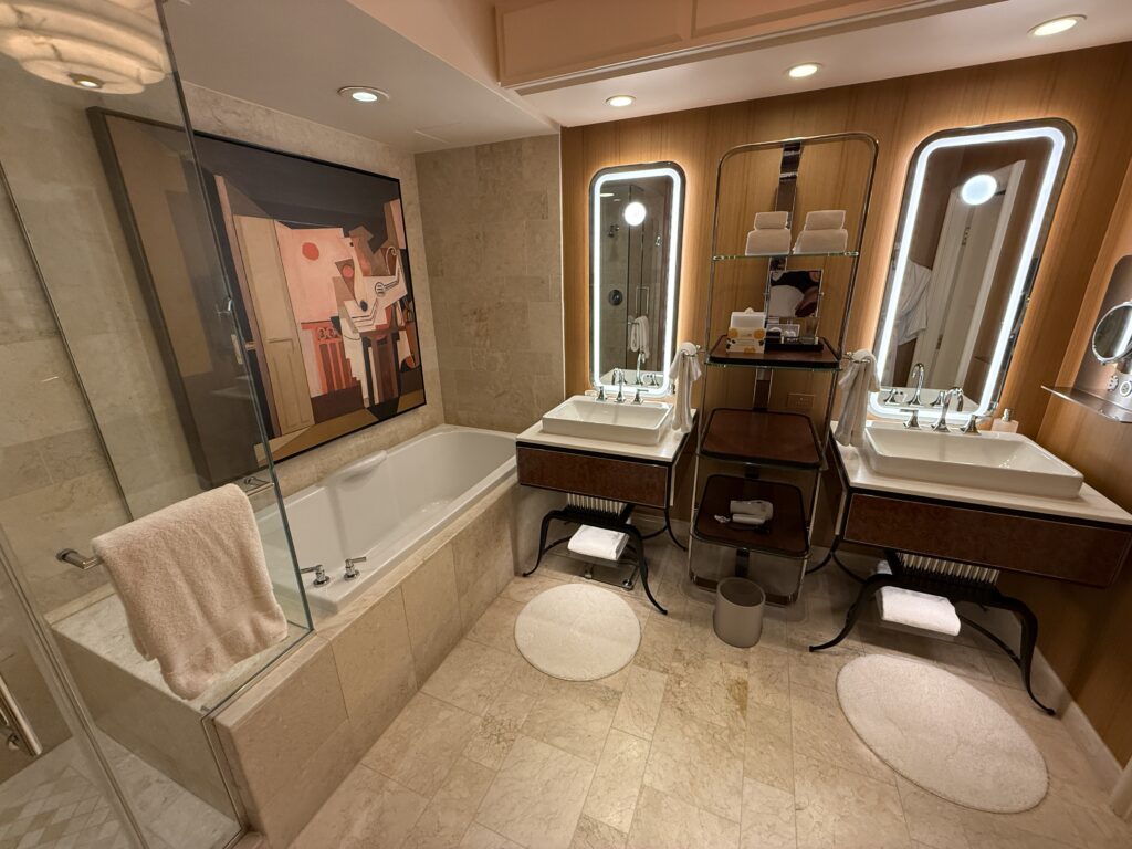 A split vanity, with two separatew illuminated mirrors. To the left is the tub and separate shower. 