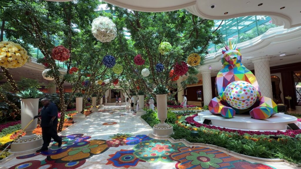 A  path leading underneath a row of illuminated trees. To the right is a giant multicolor statue of a bear. 