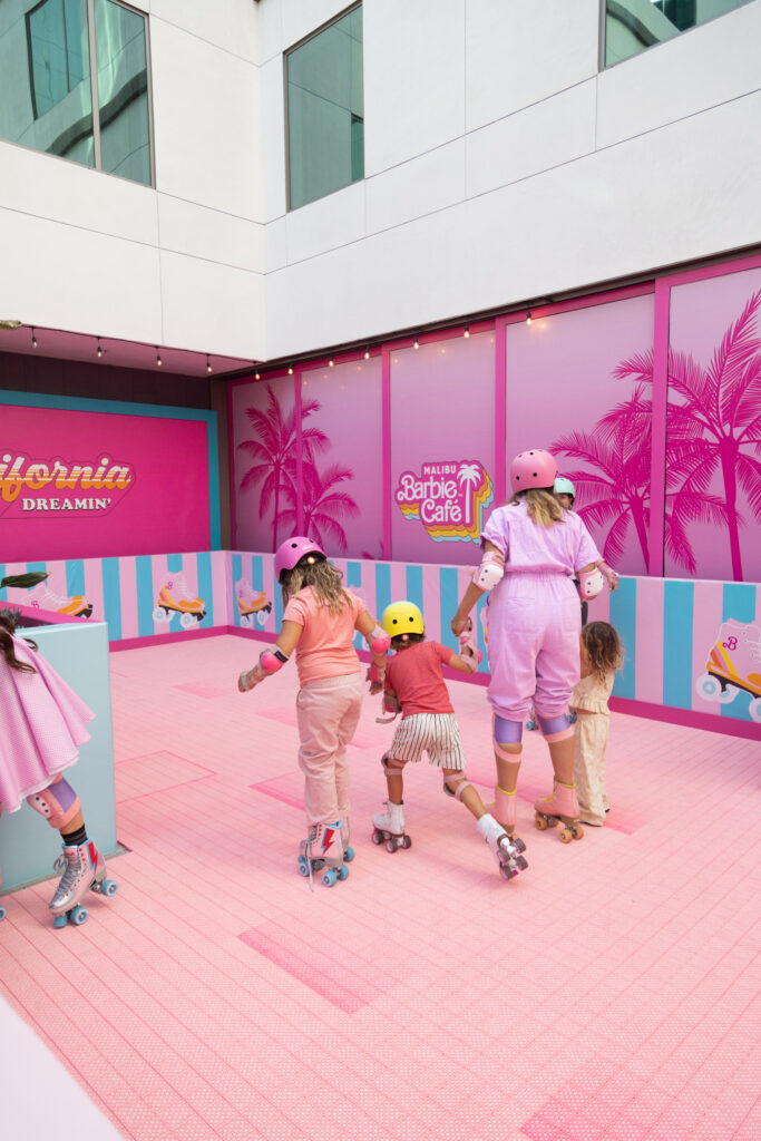 A family is holding hands , rollerskating on a pink surface.