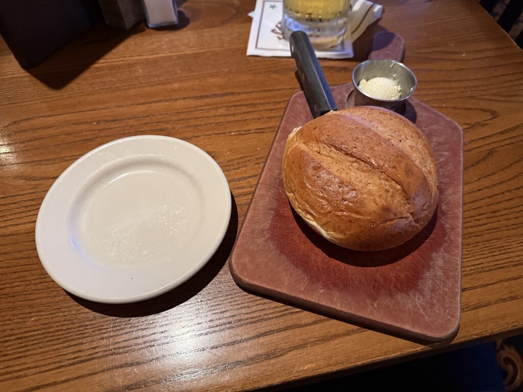 A round loaf of bread on a cutting board next to an empty white plate.