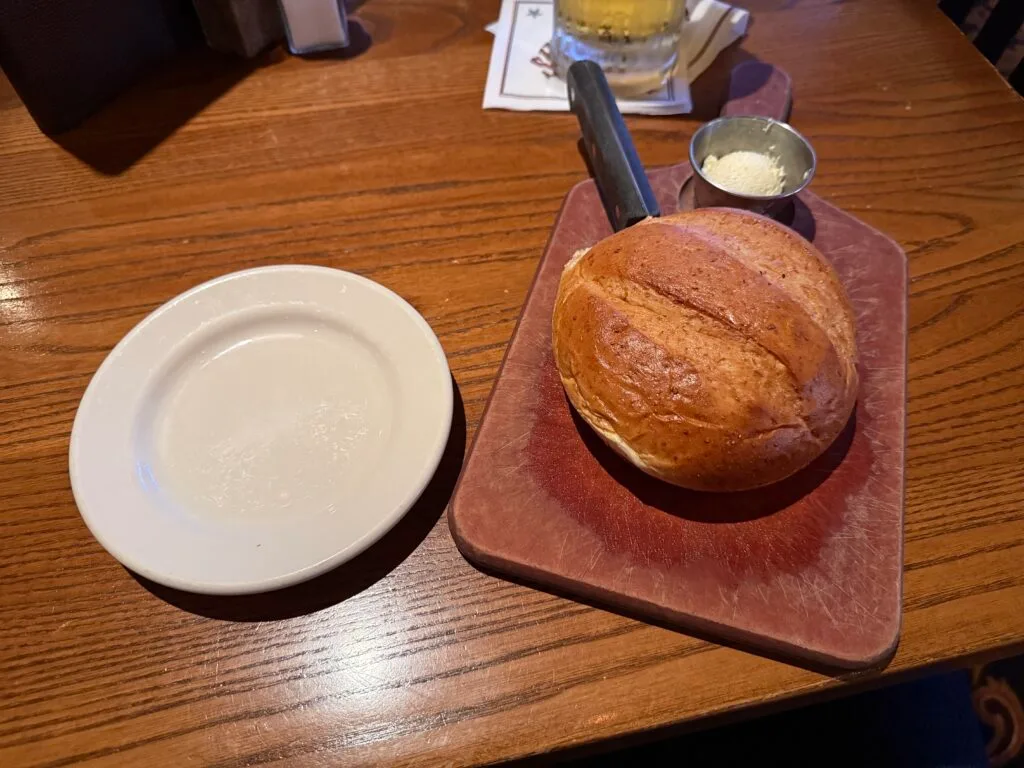 A round loaf of bread on a cutting board next to an empty white plate. 