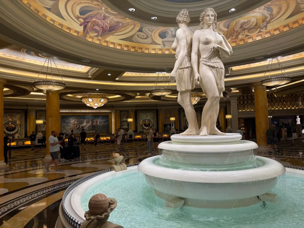 A fountain with a statue of 3 women carved from marble standing back to back.