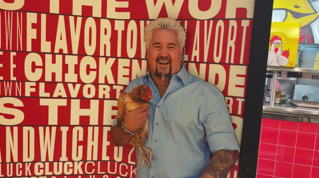 A photo op cutout of Guy Fieri holding a live chicken.