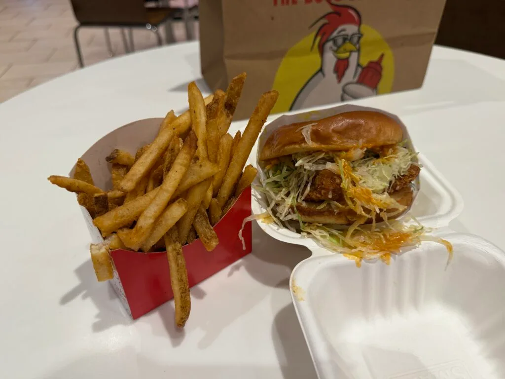 French fries in a container next to a chicken sandwich with stringy lettuce spilling out.