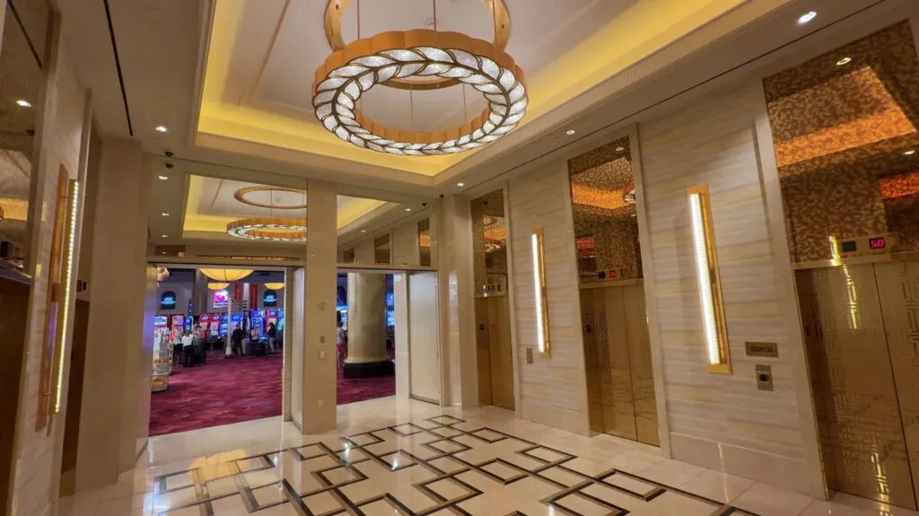 An elevator lobby with gold accents and a roman themed chandelier above.