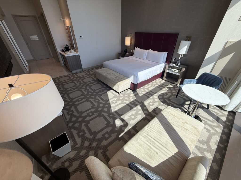 A 3rd angle of the room that shows the king bed with the hallway leading to the door and bathroom in the background.