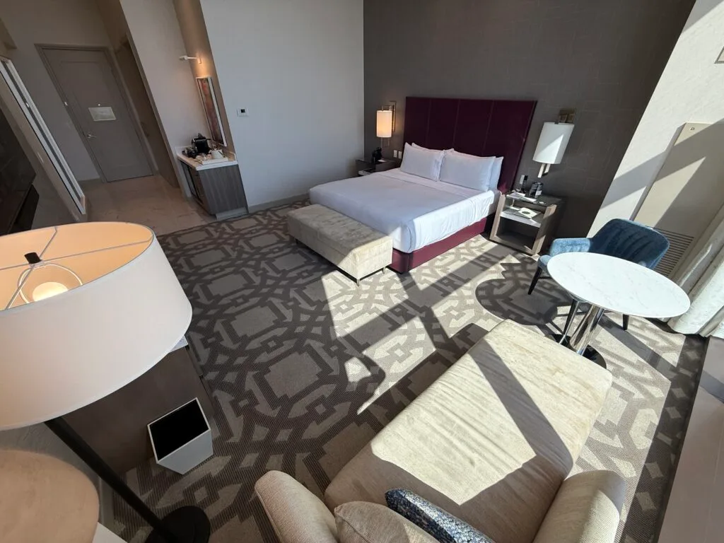 A 3rd angle of the room that shows the king bed with the hallway leading to the door and bathroom in the background. 