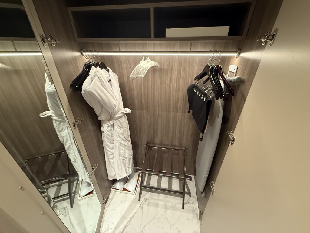 Robes hanging in an illumnated closet with slippers underneath.