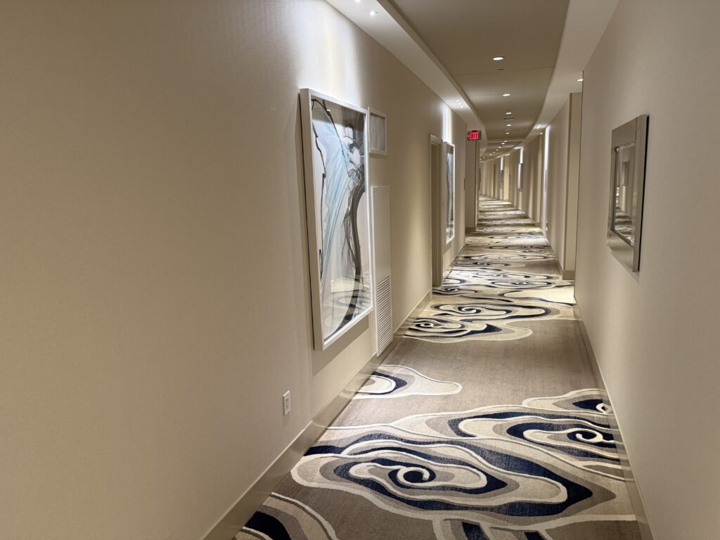 A well lit hotel hallway with illuminated artwork on the walls and high ceilings.