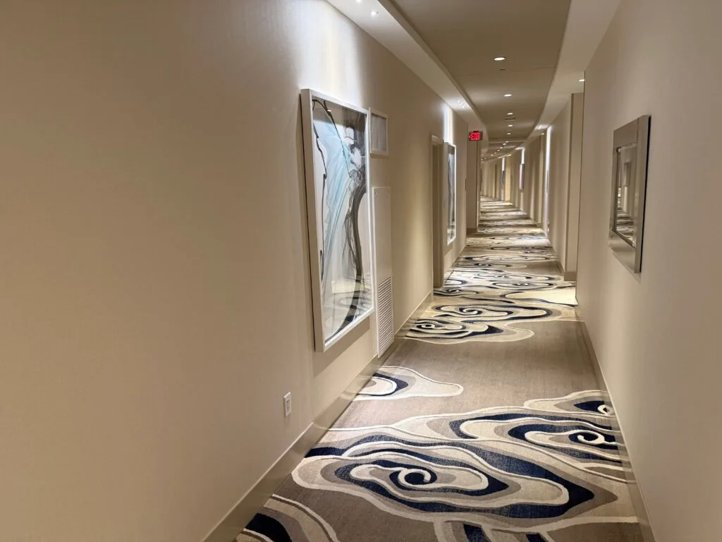 A well lit hotel hallway with illuminated artwork on the walls and high ceilings. 