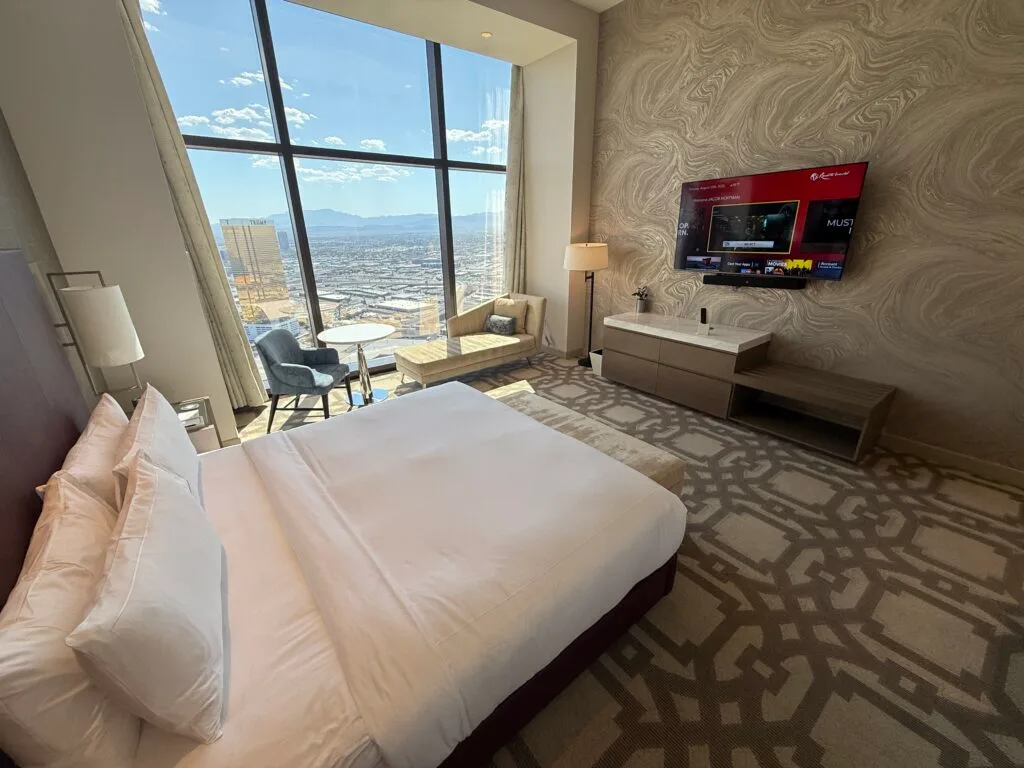 Another angle of the room that shows the TV the bed is pointed at with the open windows showing blue skies in the background. 