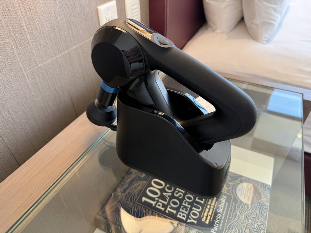 A message gun, charging bedside on an endtable.