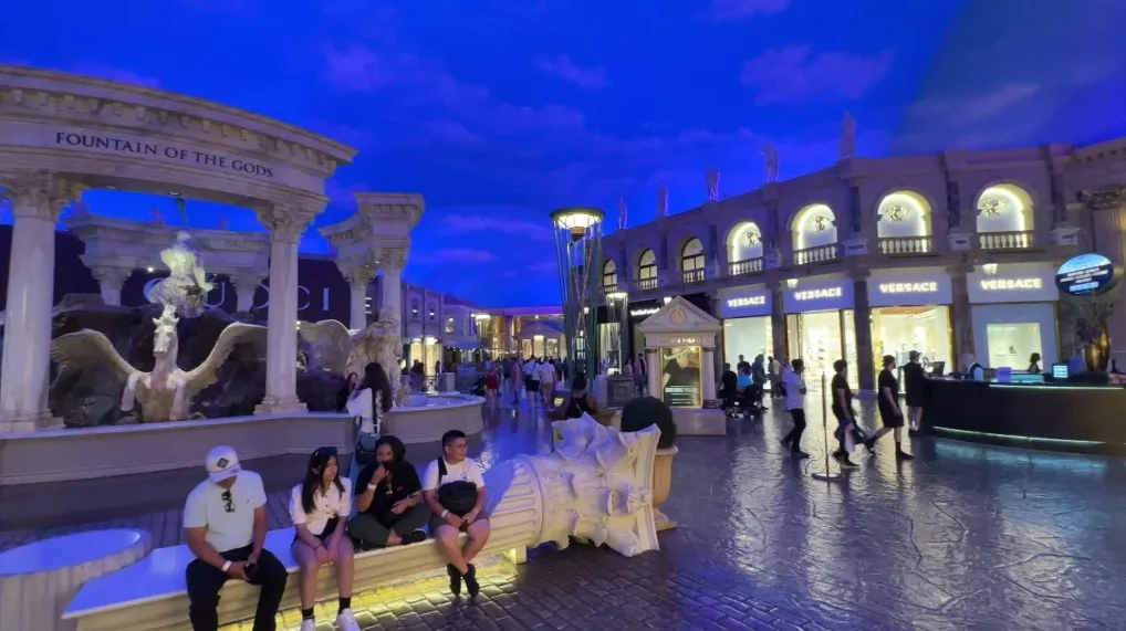 A roman themed section of the Forum Shops with statues, a fountain, and blue skies.