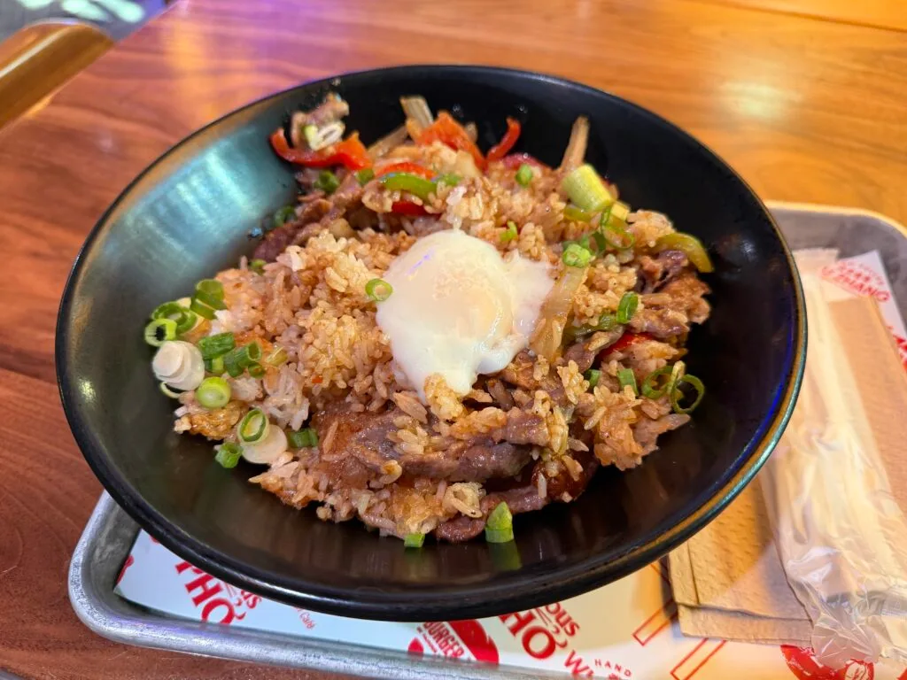 A rbowl of rice, veggies, and meat with a fried egg atop it. 