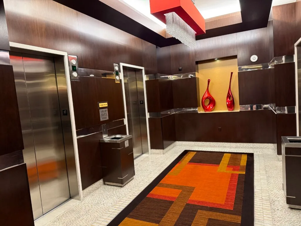 Ground floor elevator lobby, which has decorative overhead lighting, dark wood features, and vases on display in the background. 