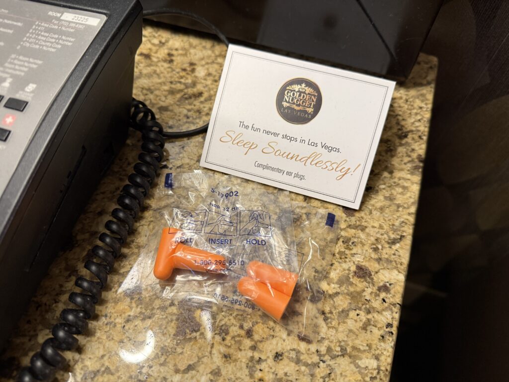 A pair of orange earplugs ominously set on the endtable next to the bed.