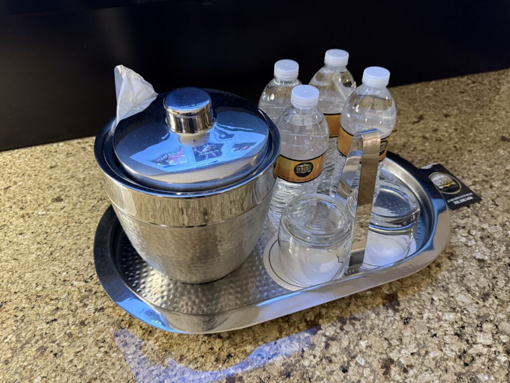 4 full sized bottles of water sit on a metal tray next to a metal ice bucket.