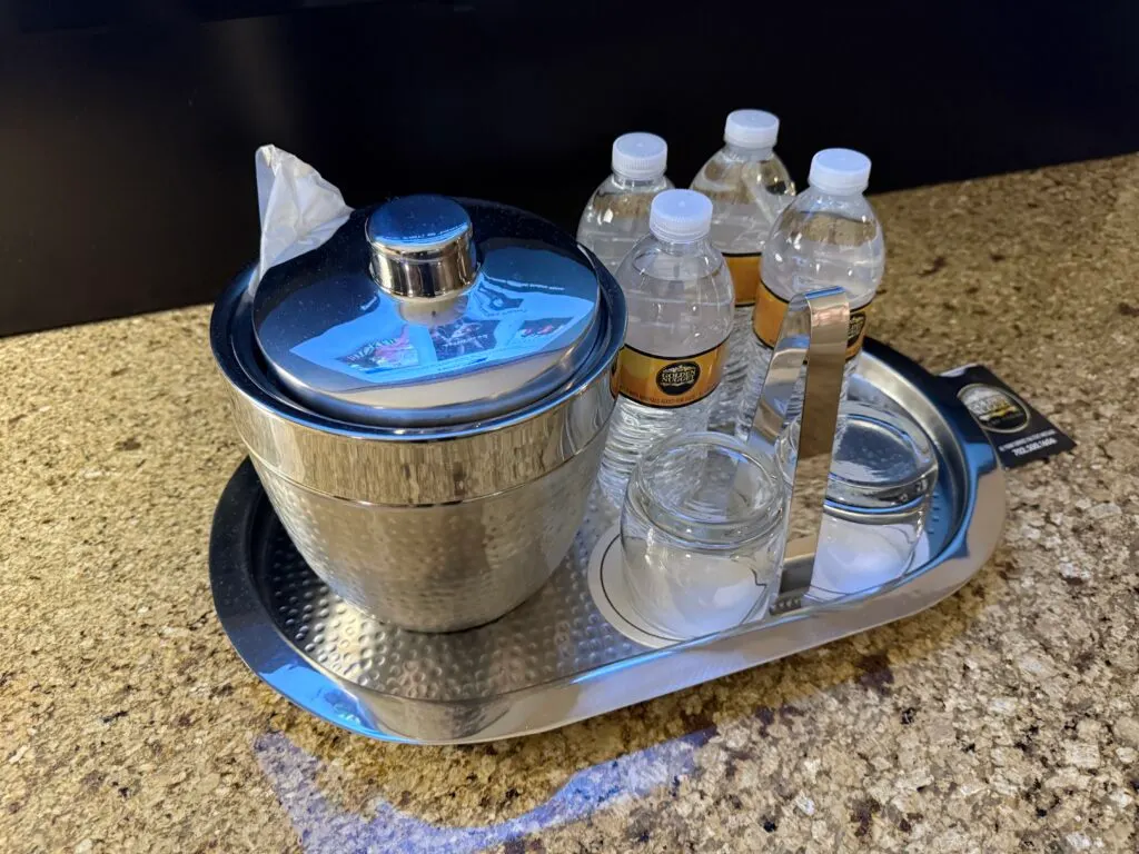 4 full sized bottles of water sit on a metal tray next to a metal ice bucket. 