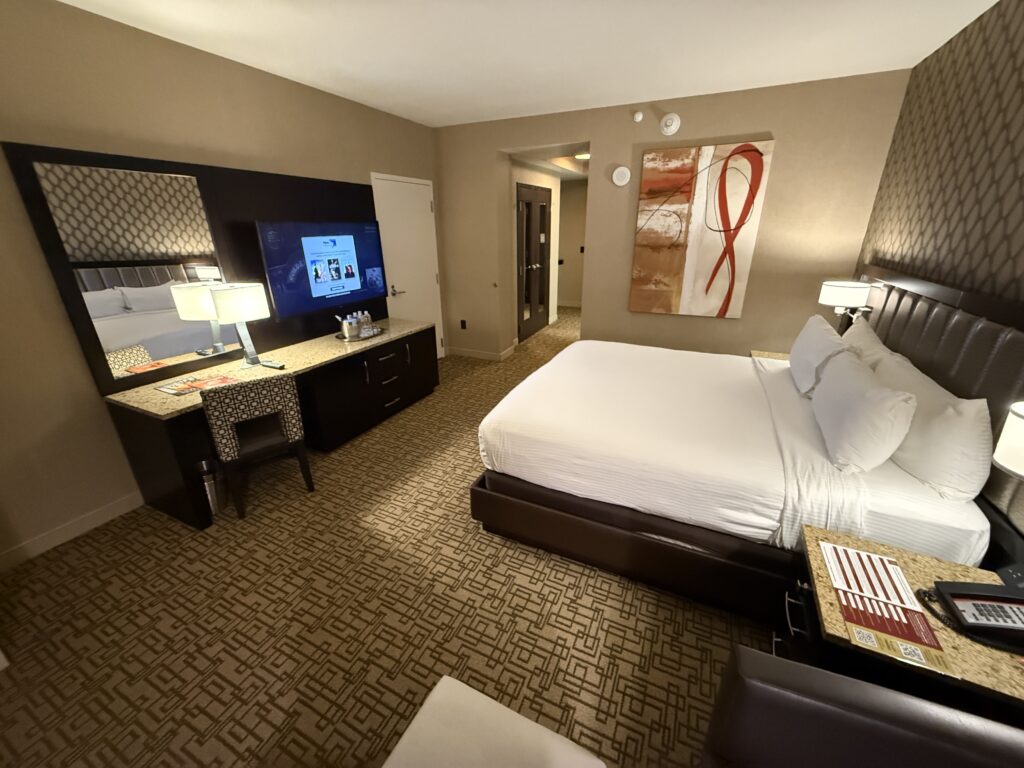 the king bed pointing at the TV with a paintint on the wall beside the bed with "swirly" patterns.