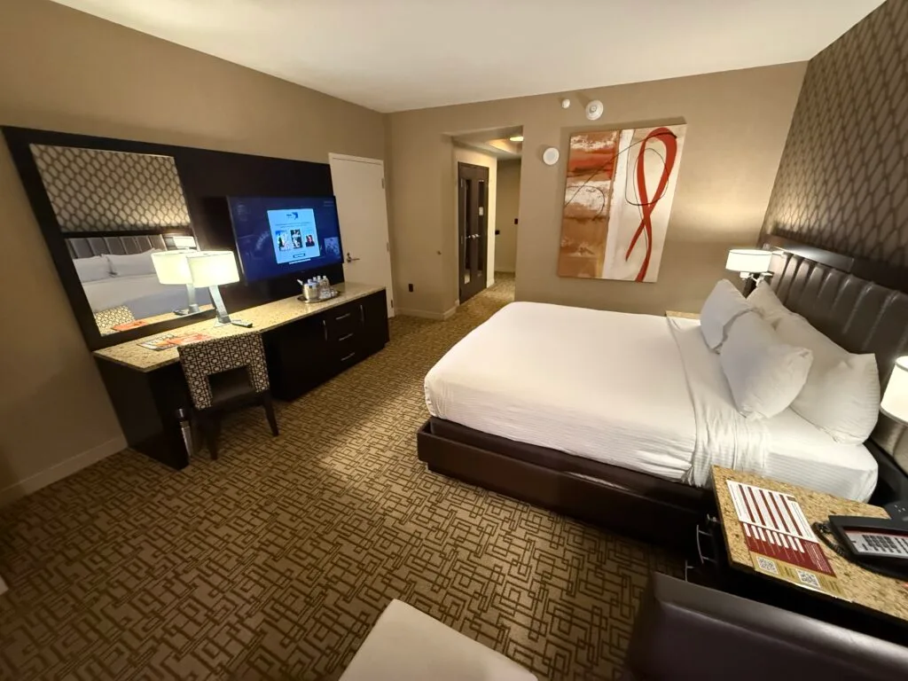 the king bed pointing at the TV with a paintint on the wall beside the bed with "swirly" patterns. 