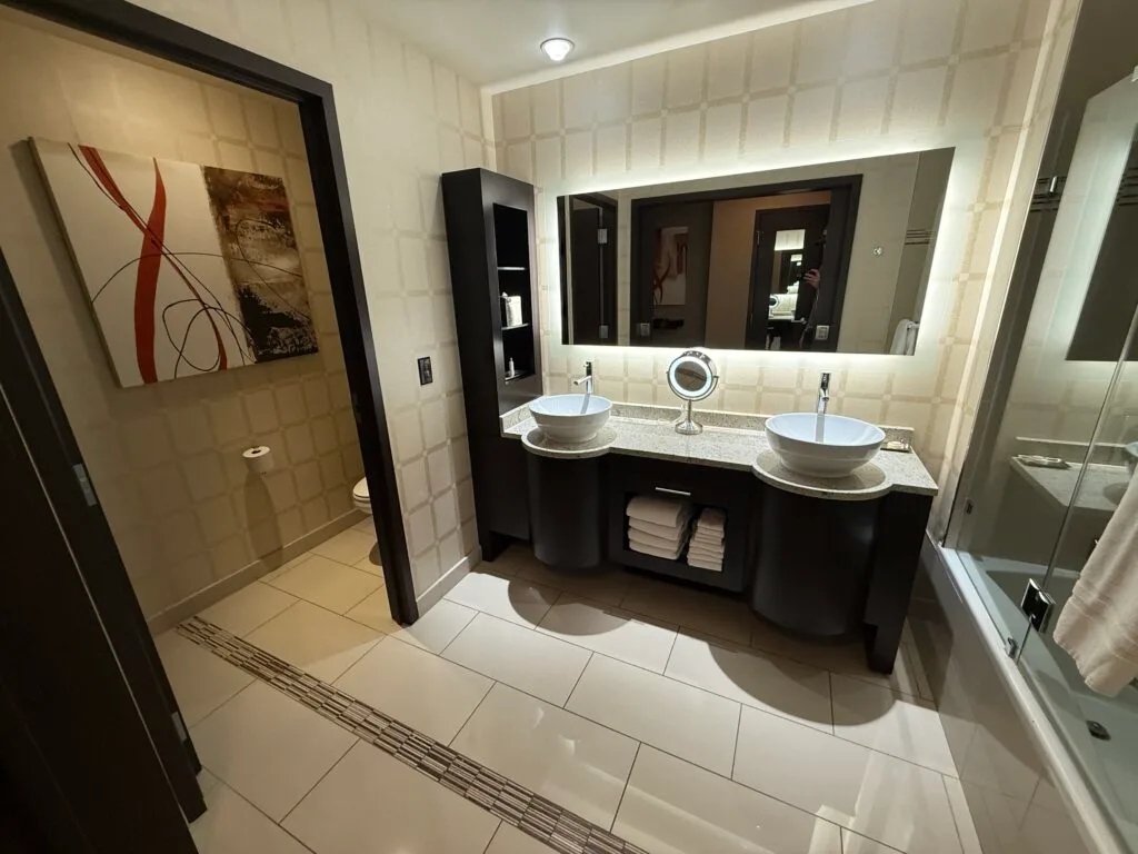 A dual sink vanity with a doorway to the toilet to the left. 