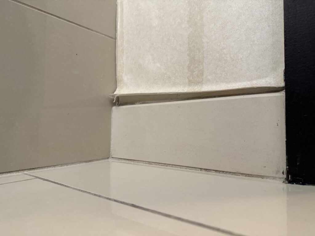 A small section of peeling wallpaper above the baseboard near the tub.