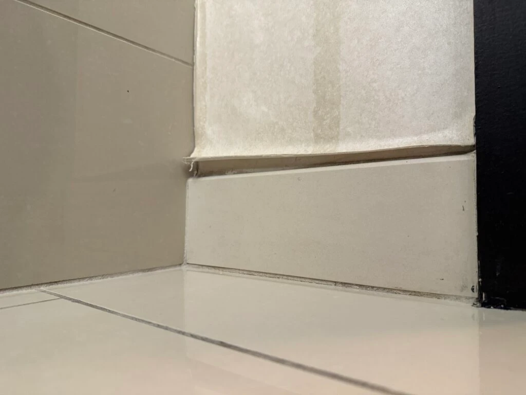 A small section of peeling wallpaper above the baseboard near the tub. 