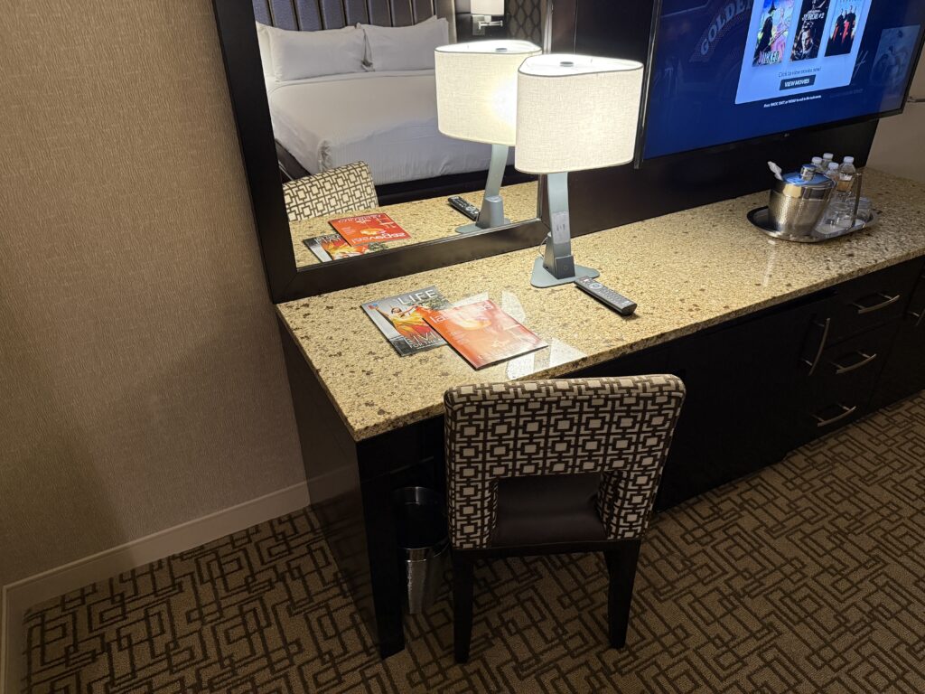 A small workdesk, with 2 magazines atop it alongside a touch activated lamp with wireless charging.