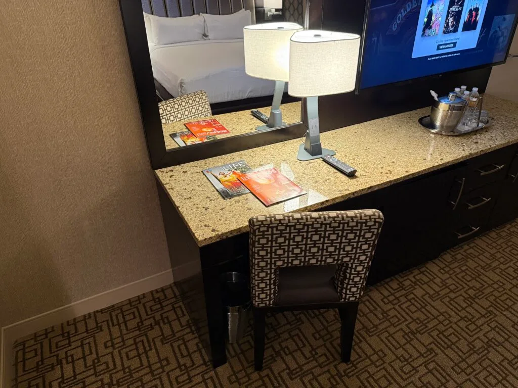 A small workdesk, with 2 magazines atop it alongside a touch activated lamp with wireless charging. 