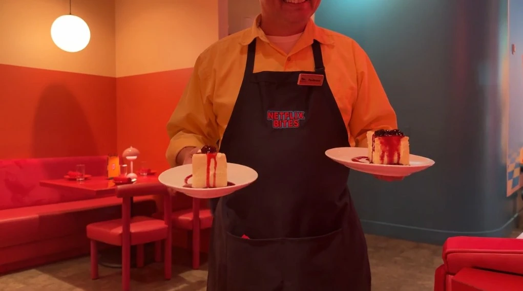 A waiter holding two plates of cheesecake, which look identical.